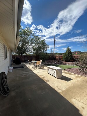 A covered patio with outdoor furniture, a covered table, and a view of a backyard with a tree and a stop sign. - Great 3 bedroom home for outdoor enthusiasts and families! (Mancos)
