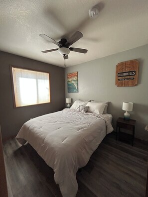 A bedroom with a bed, a ceiling fan, a window with blinds, a wall clock, and a wall-mounted lamp. - Great 3 bedroom home for outdoor enthusiasts and families! (Mancos)
