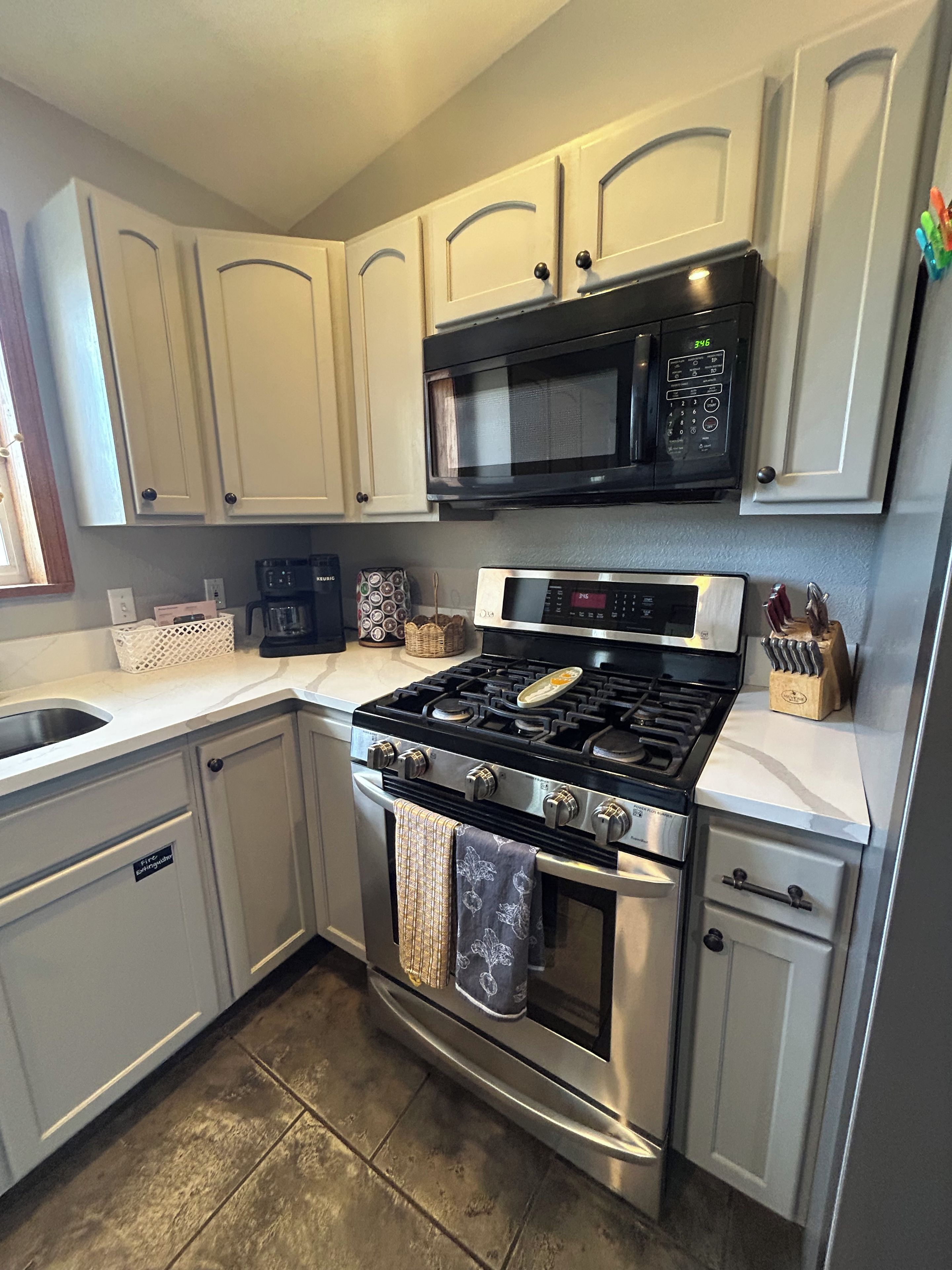 A kitchen with white cabinets, a black microwave, a stainless steel stove, and a coffee maker.