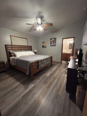 A bedroom with a wooden bed, a ceiling fan, a nightstand, a desk with a computer, and a mirror. - Great 3 bedroom home for outdoor enthusiasts and families! (Mancos)