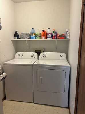A laundry room with two front-loading washing machines and a shelf above containing various cleaning products. - Great 3 bedroom home for outdoor enthusiasts and families! (Mancos)