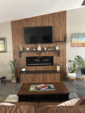 A living room with a flat-screen TV mounted on a wooden wall, a coffee table with books and remotes, and potted plants. - Great 3 bedroom home for outdoor enthusiasts and families! (Mancos)
