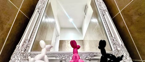 A bathroom with a large ornate mirror, a white and pink sculpture, and a black sculpture on the floor.