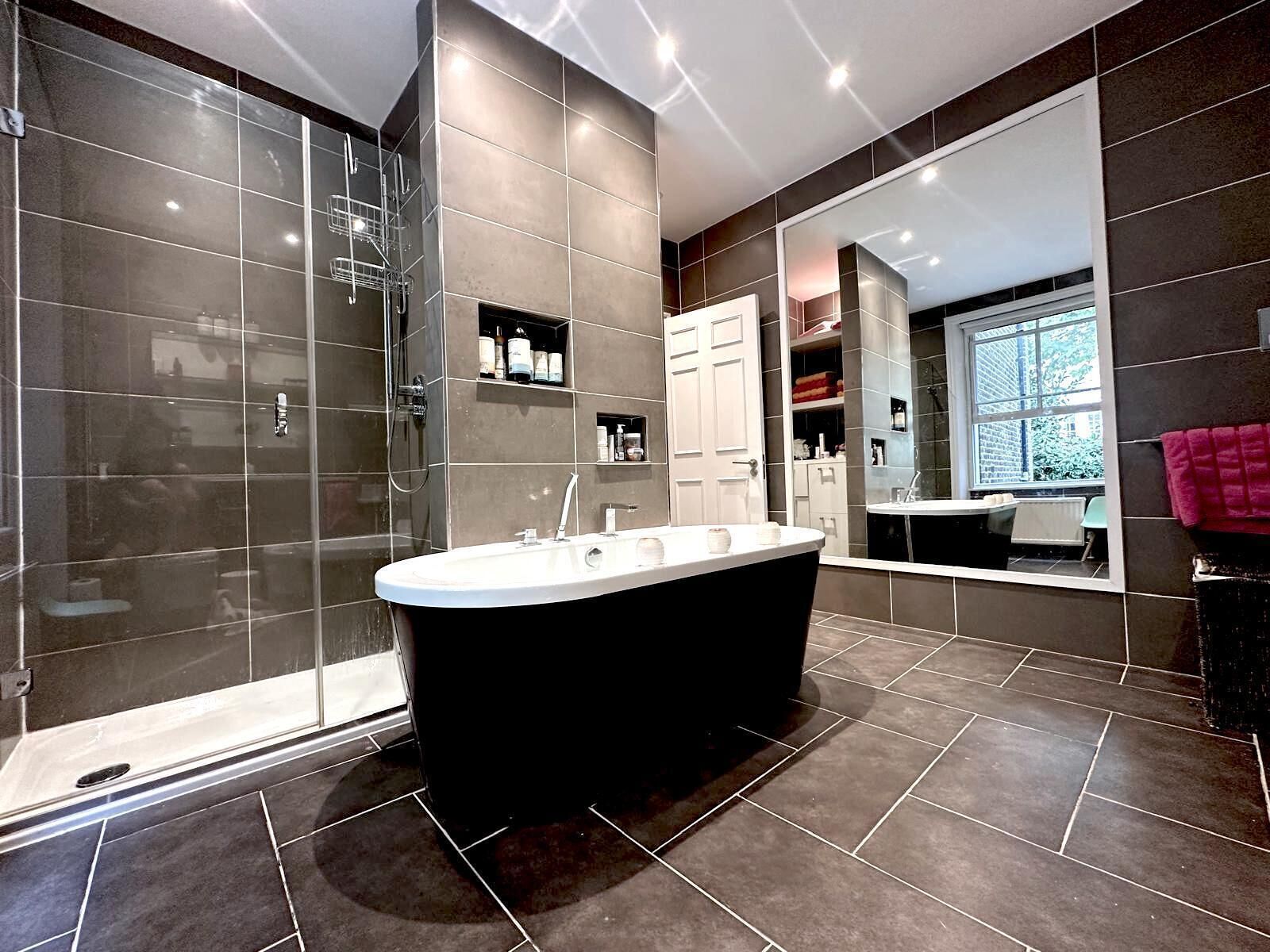 A modern bathroom with a freestanding bathtub, a glass shower enclosure, and a large mirror reflecting the room.