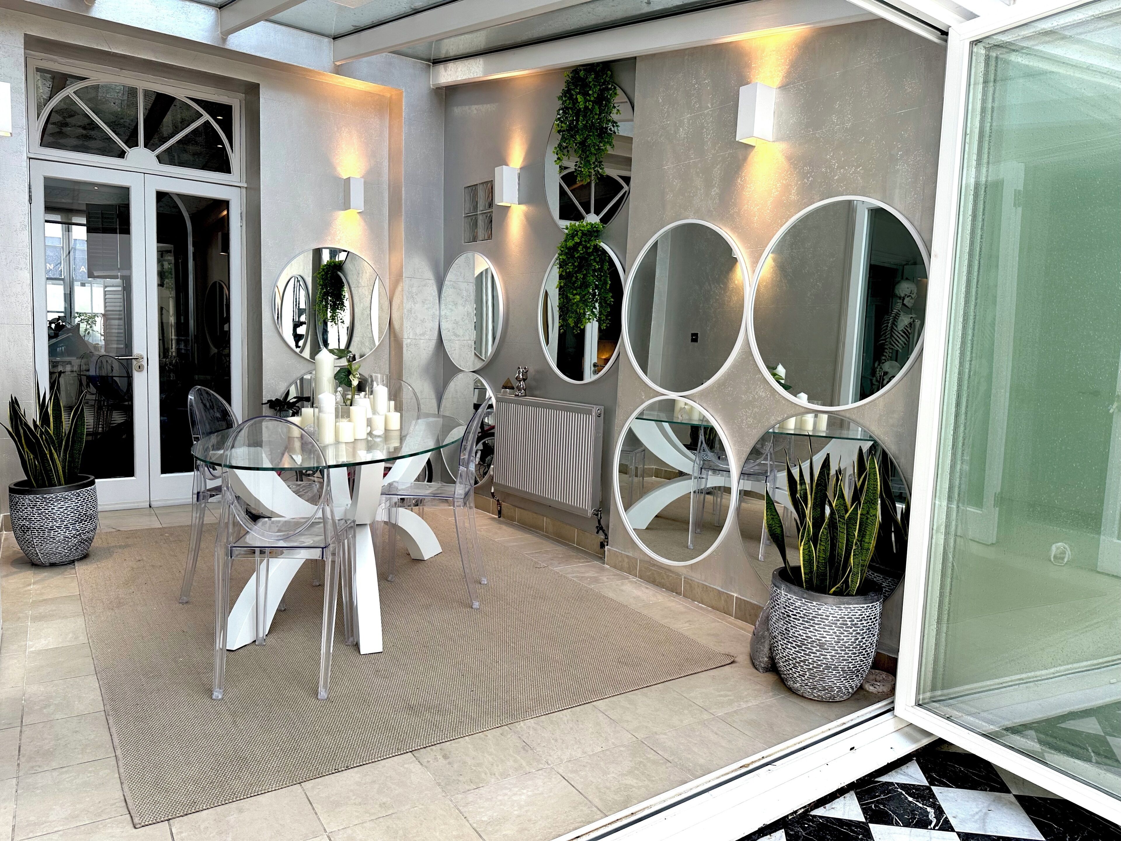 A modern dining area with a glass table, clear chairs, and multiple wall-mounted mirrors.