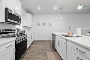 A modern kitchen with white cabinetry, stainless steel appliances, and a central island with a sink.
