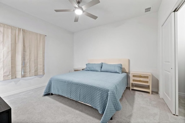 A bedroom with a bed, nightstands, a ceiling fan, and a wardrobe.
