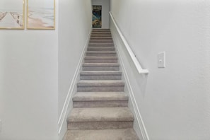 A carpeted staircase with a white handrail, leading to a landing where a poster is visible.
