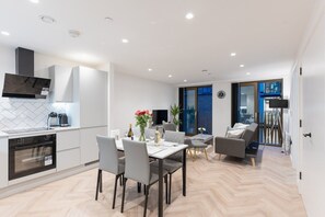 A modern kitchen with built-in appliances, a dining area with a table and chairs, and a living space with a sofa and a TV. - One bed flat 7 mins walk to Manchester Piccadilly (Greater Manchester)