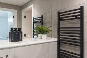 A bathroom with a white countertop, black towel racks, a potted plant, and bottles of body wash and shampoo. - One bed flat 7 mins walk to Manchester Piccadilly (Greater Manchester)