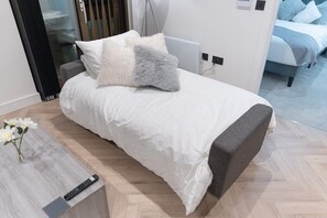 A neatly made bed with a grey headboard, a remote control on a side table, and a vase with white flowers. - One bed flat 7 mins walk to Manchester Piccadilly (Greater Manchester)