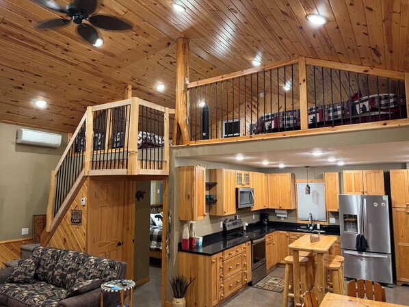 A cabin interior with a wooden staircase, a kitchen with modern appliances, and a living area with a sofa.