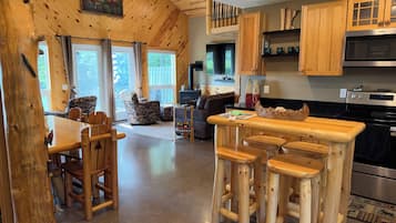 A wooden interior with a dining area, bar stools, and a kitchen with wooden cabinets and appliances.