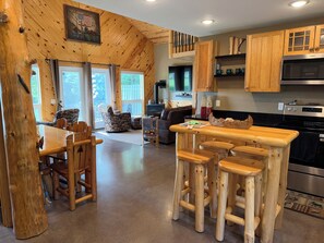 A wooden interior with a dining area, bar stools, and a kitchen with wooden cabinets and appliances.