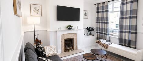 A modern living room with a fireplace, a sofa, a TV, and a window with curtains.