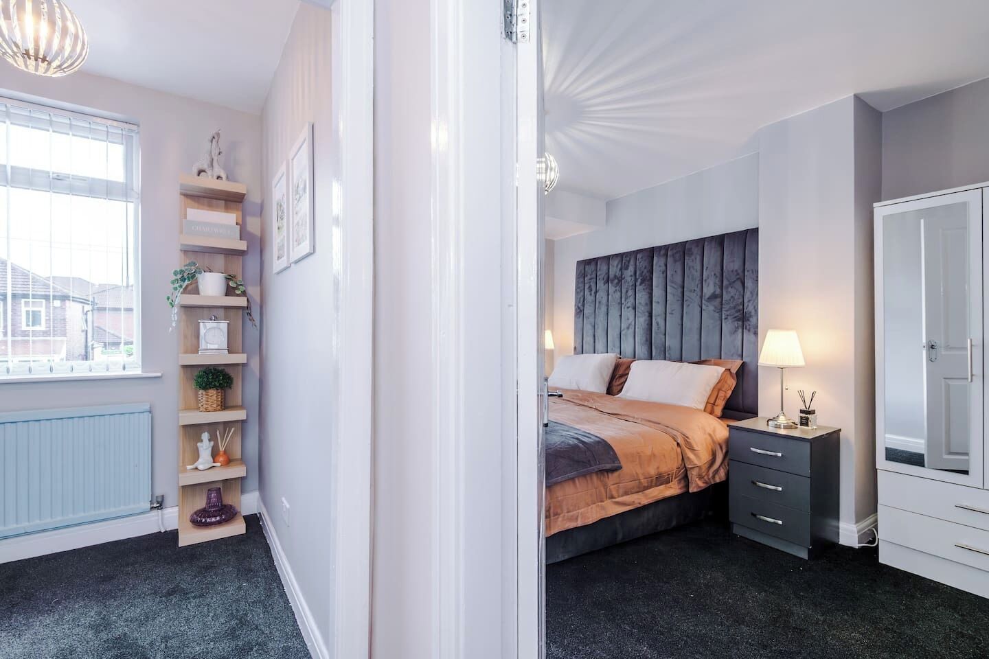 Een slaapkamer met een bed, nachtkastje, lamp, kledingkast en een raam met jaloezieën.