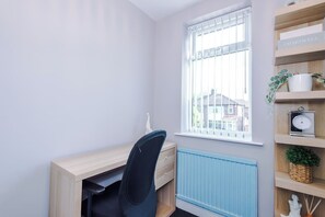 A room with a desk, chair, radiator, window with blinds, and a shelf with decorative items. - 3 bed house · Driveway · EV Charger · Sleeps 7 (Greater Manchester)