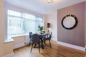 A dining area with a round table, chairs, a potted plant, and a wall-mounted mirror. - 3 bed house · Driveway · EV Charger · Sleeps 7 (Greater Manchester)