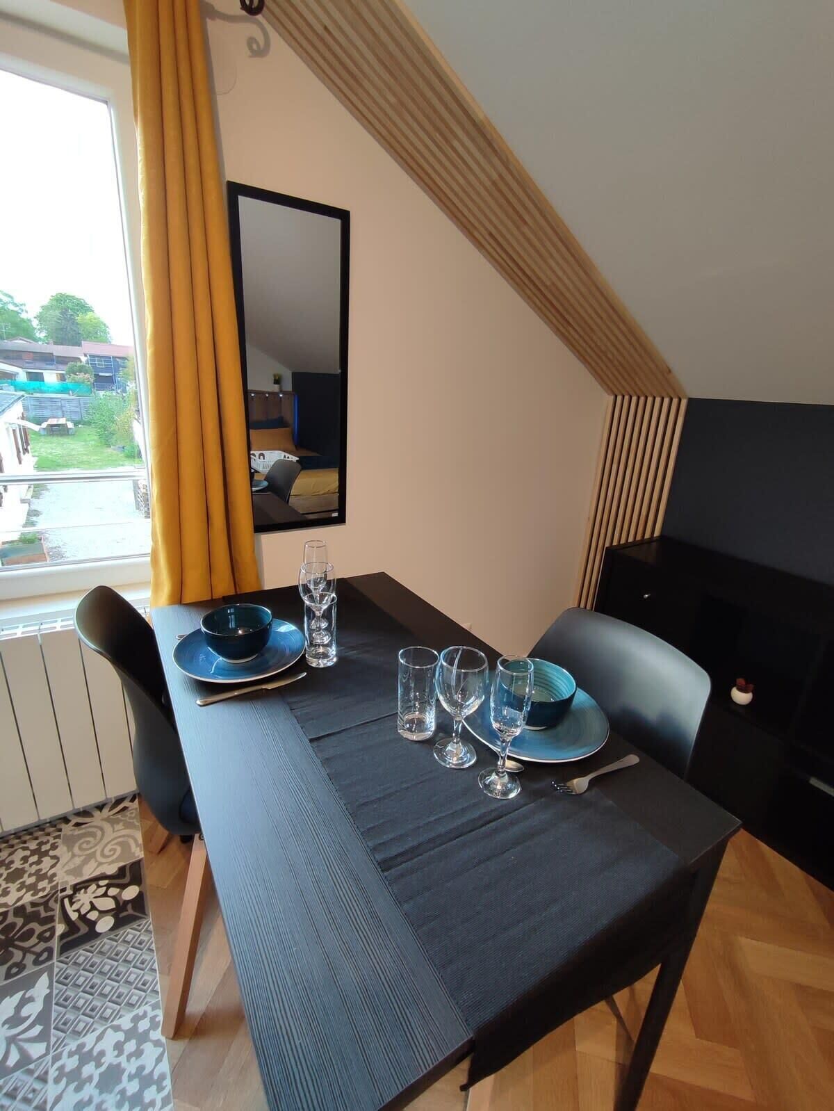 Un coin repas avec une table dressée pour deux personnes, un miroir au mur et une vue sur l’extérieur.