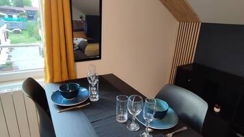 Un coin repas avec une table dressée pour deux personnes, un miroir au mur et une vue sur l’extérieur.