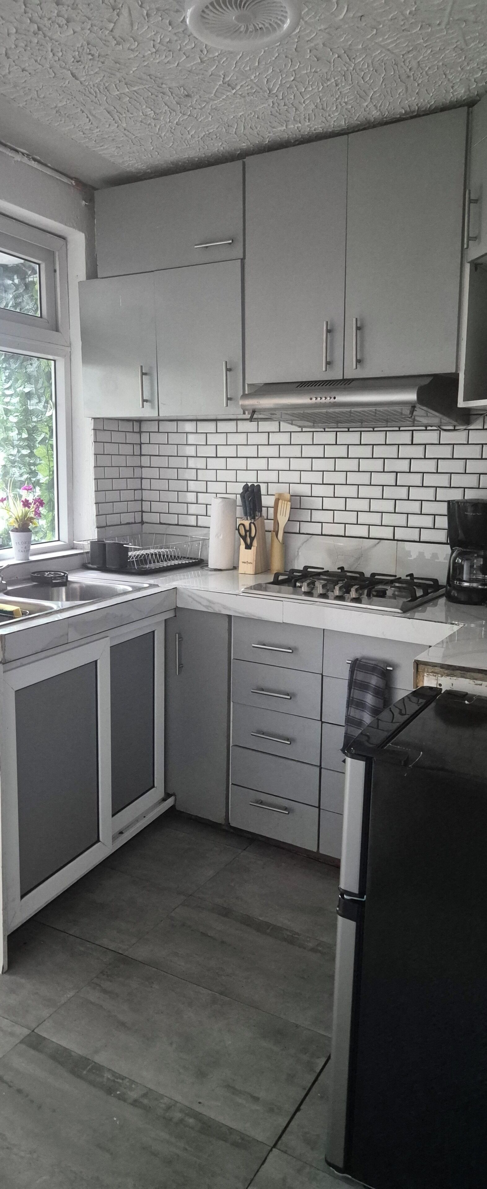 A kitchen with grey cabinets, a tiled backsplash, a stove, and a refrigerator.