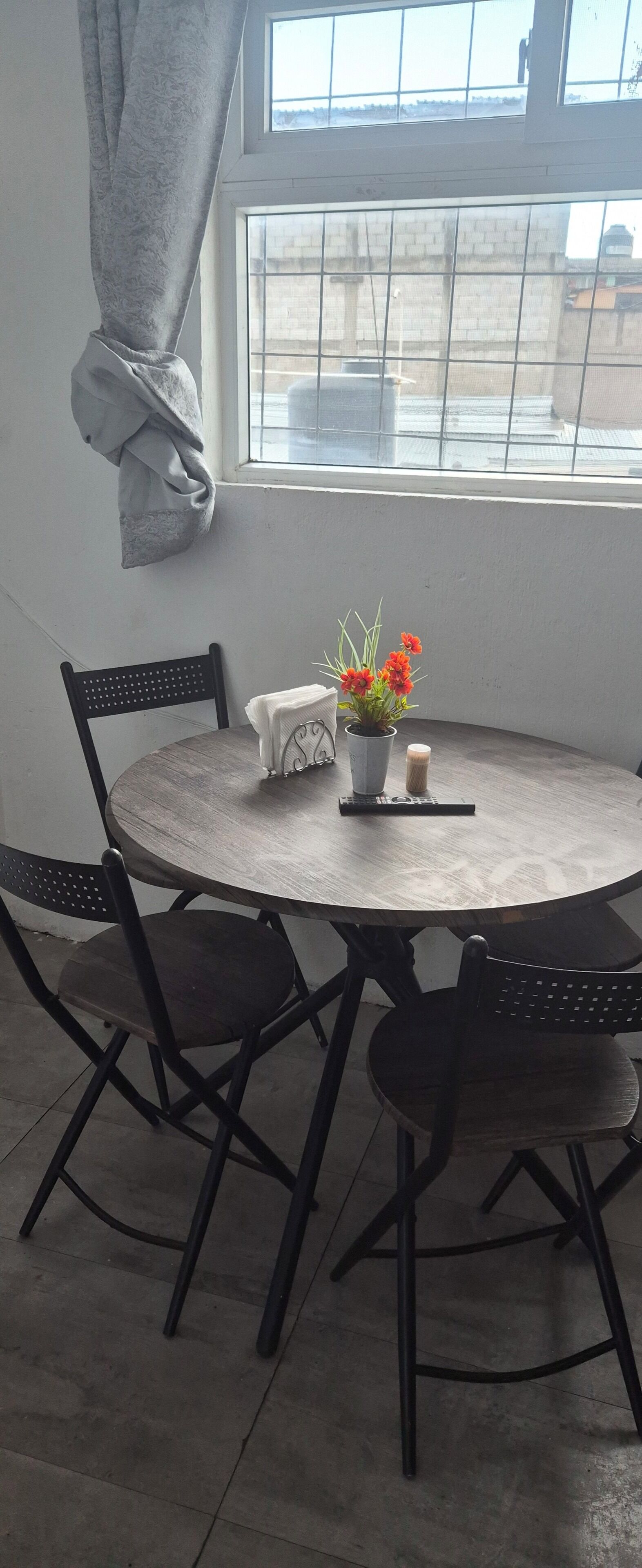A round table with four chairs, a potted plant with flowers, a remote control, and a candle on a windowsill.