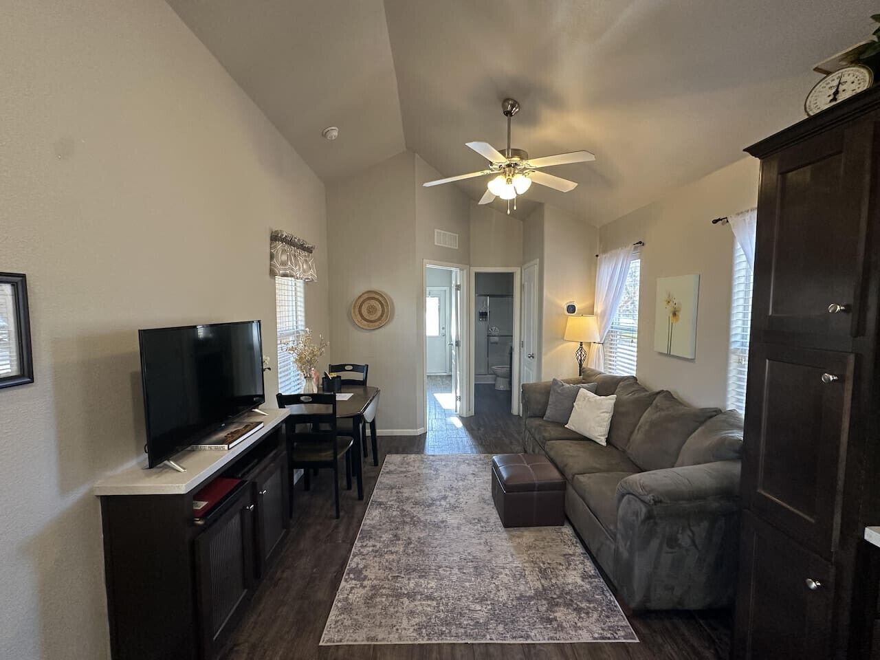 A living room with a television, a ceiling fan, a sofa, and a dining area with a table and chairs.
