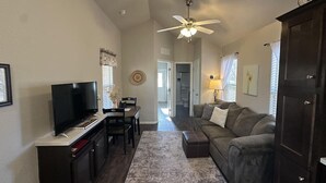 A living room with a television, a ceiling fan, a sofa, and a dining area with a table and chairs.