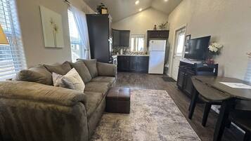 A compact living space with a sofa, ottoman, dining table, and kitchen area.