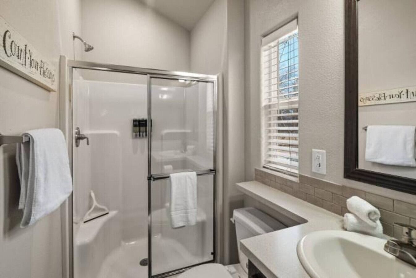 A bathroom with a glass shower enclosure, a sink, and a mirror.