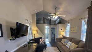 A living room with a dining table, a sofa, a ceiling fan, and a staircase leading to an upper level.