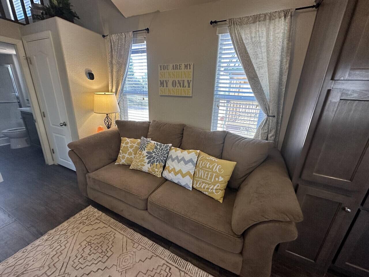 A living room with a brown sofa, patterned cushions, a rug, and a wall sign.