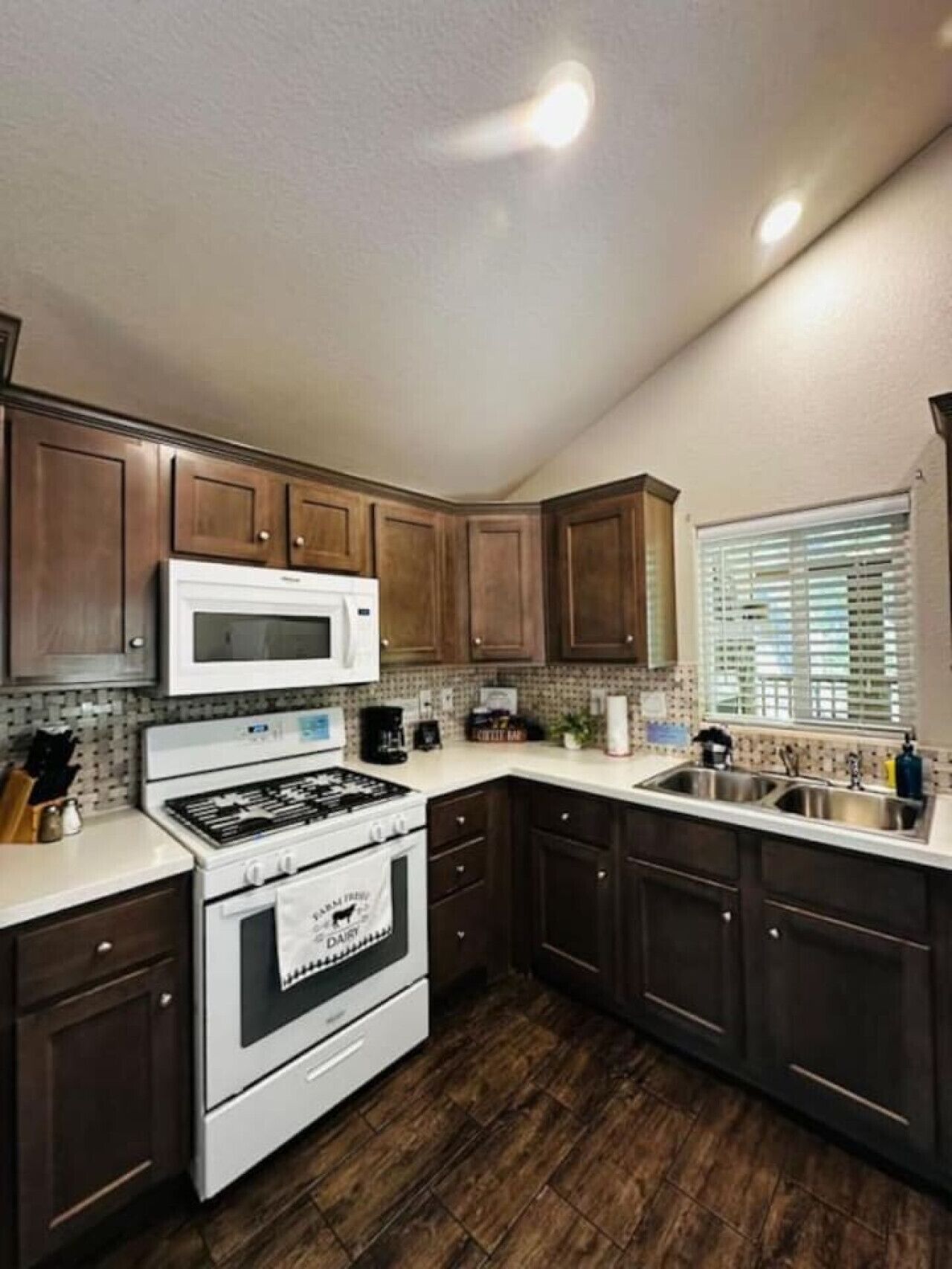 A kitchen with dark wooden cabinets, a white stove, a microwave, and a window with blinds.