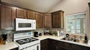 A kitchen with dark wooden cabinets, a white stove, a microwave, and a window with blinds.