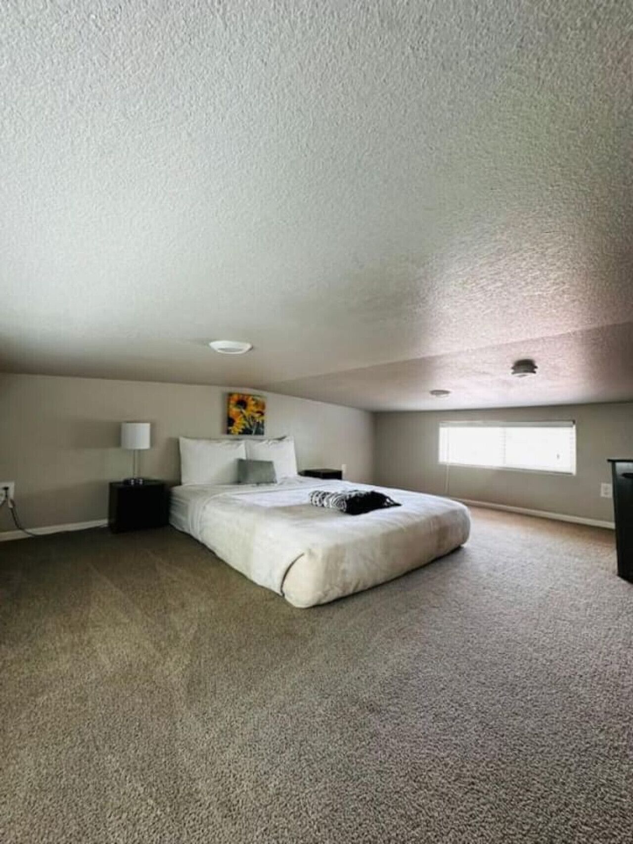 A bedroom with a single bed, a nightstand, a lamp, and a painting on the wall.