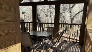 A covered outdoor seating area with a table and chairs, wooden flooring, and a view of bare trees.