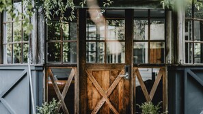 Une porte en bois rustique, dotée d’un loquet en métal, qui donne accès à un bâtiment comportant de nombreuses fenêtres.