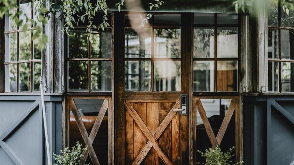 A rustic wooden gate with a metal latch, leading to a building with multiple windows.