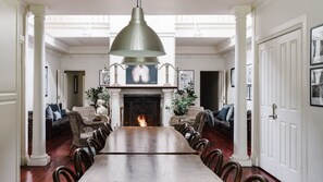 A dining room with a long table, chairs, a fireplace, and a hanging light fixture.