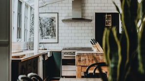 Una cocina con paredes de azulejos blancos, una campana extractora de acero inoxidable, una encimera de madera y un juego de cuchillos.