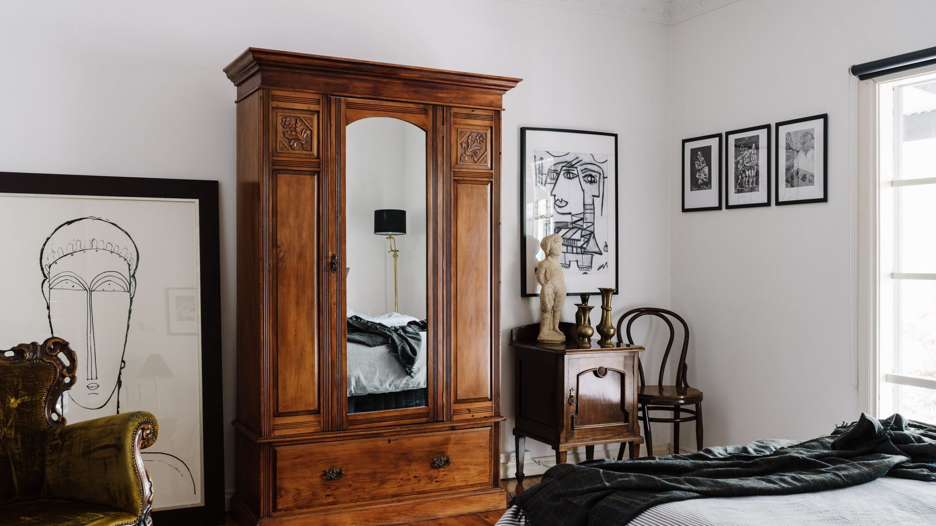 Un dormitorio con un armario de madera, una cama, una silla y obras de arte en las paredes.