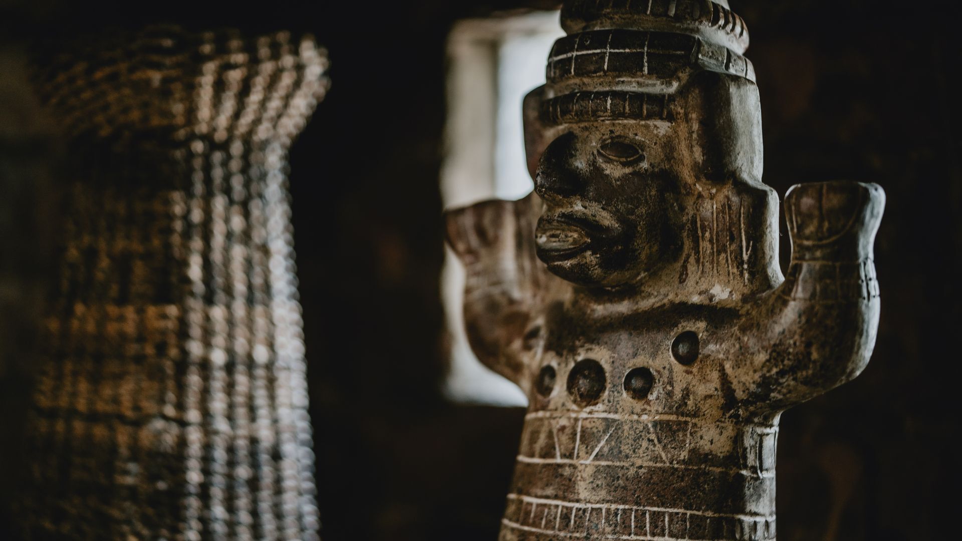 Een close-up van een verweerd, mogelijk historiek artefact met een gezicht en pijp, voor een donkere achtergrond.