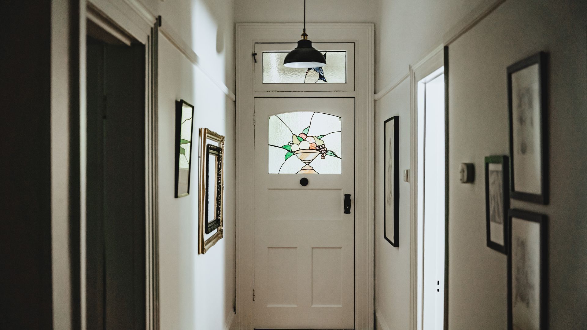 Um corredor com uma porta branca, quadros nas paredes e um candeeiro suspenso.