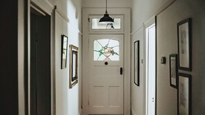 Un couloir avec une porte blanche, des tableaux encadrés et un luminaire suspendu.