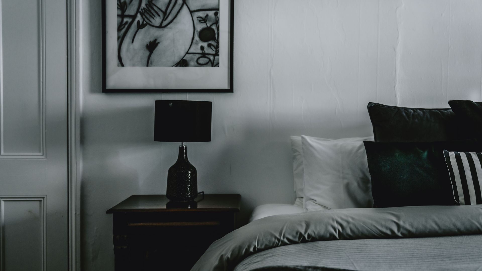 A bedroom with a bed, a nightstand, a lamp, and a framed picture on the wall.