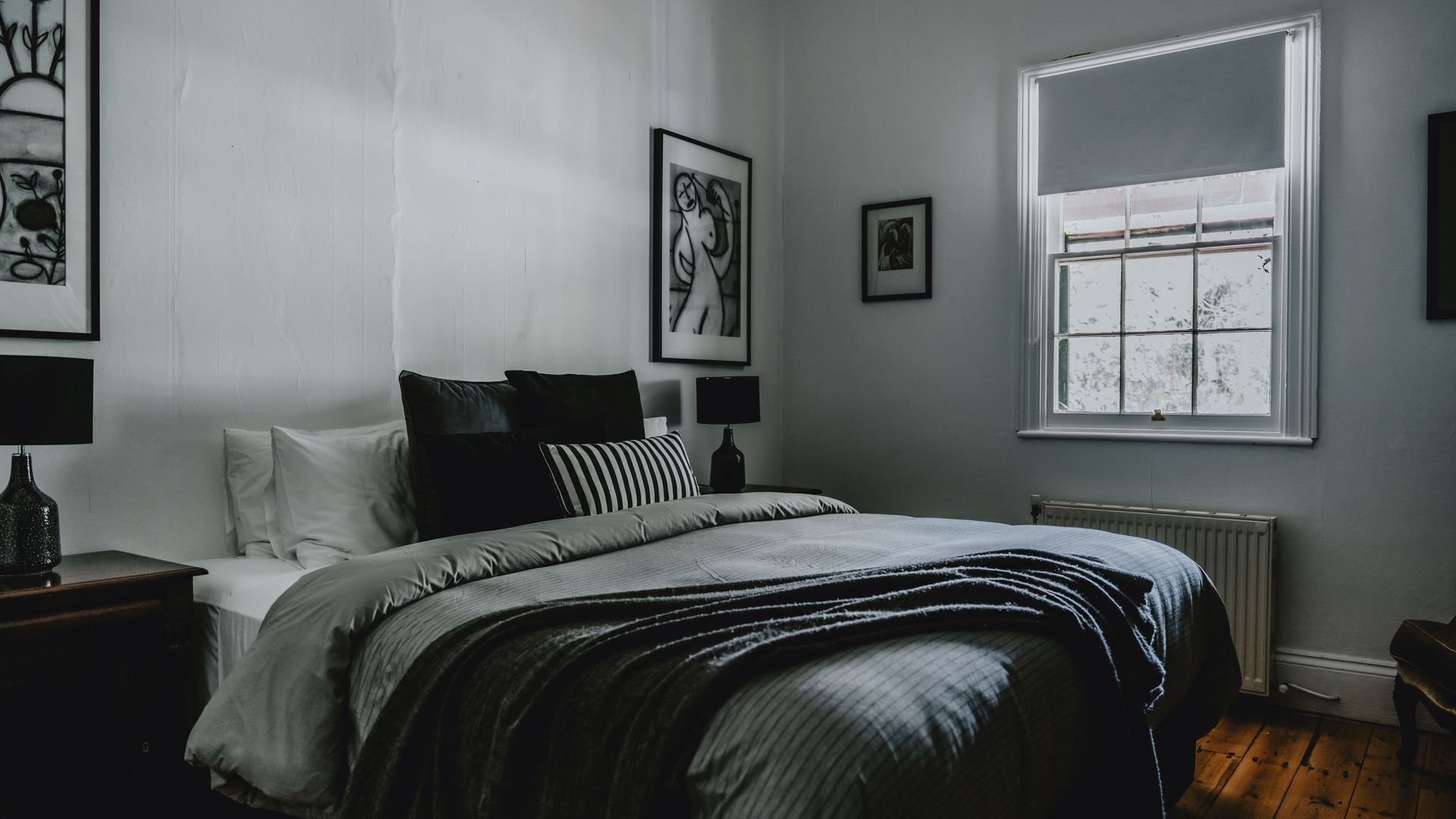 Un dormitorio con cama, mesita de noche, ventana y una obra de arte en la pared.