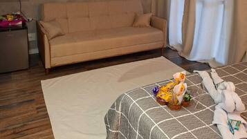 Een hotelkamer met een bank, een bed met een geruit sprei, een flatscreen televisie aan de muur en een raam met gordijnen.