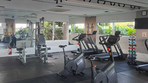 Ein Fitnessstudio mit Trainingsgeräten, großen Fenstern und einer Spiegelwand.