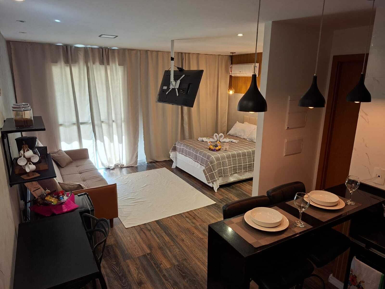 Ein Hotelzimmer mit einem Bett, einem Schreibtisch mit Stuhl, einem Esstisch mit Tellern und Gläsern, einer Couch und einem großen Fenster mit Vorhängen.