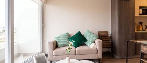 Una sala de estar moderna con un sofá color beige, dos mesas redondas blancas y vistas al exterior a través de ventanas grandes.